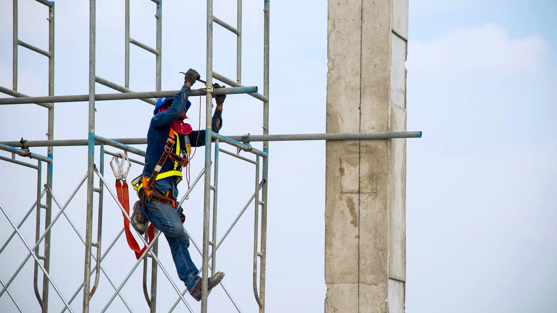 A worker using a double leg lanyard is working at height on scaffolding with safety measures.