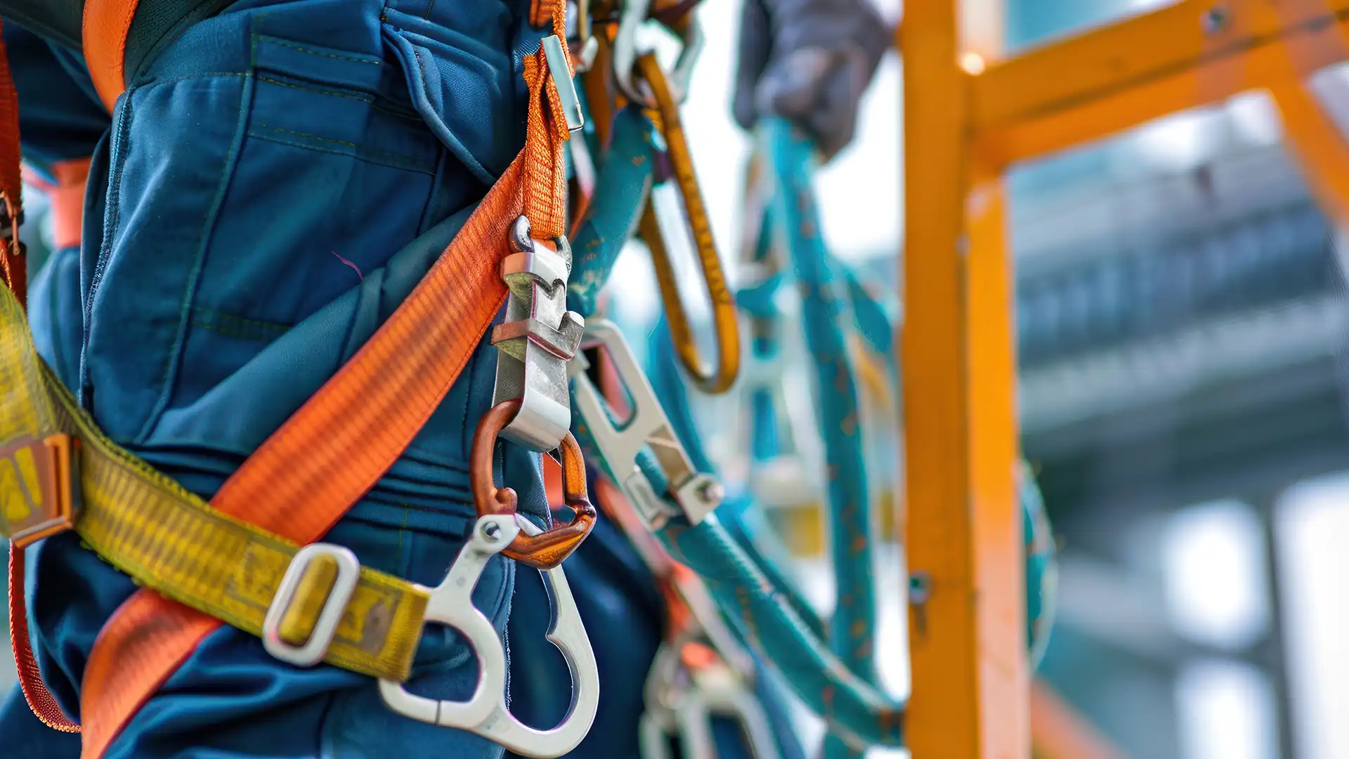 Emniyet kemeri, lanyard ve karabinalarla güvenli şekilde ankraja bağlı bir çalışanın ekipman detay görüntüsü.